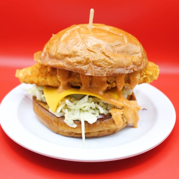 Krispi Hot Chicken sandwich with fried chicken, cheese, coleslaw, and sauce on a white plate.