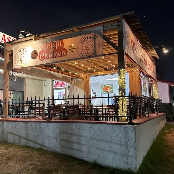 Krispi Hot Chicken restaurant exterior at night, with an illuminated patio and "OPEN" sign visible.