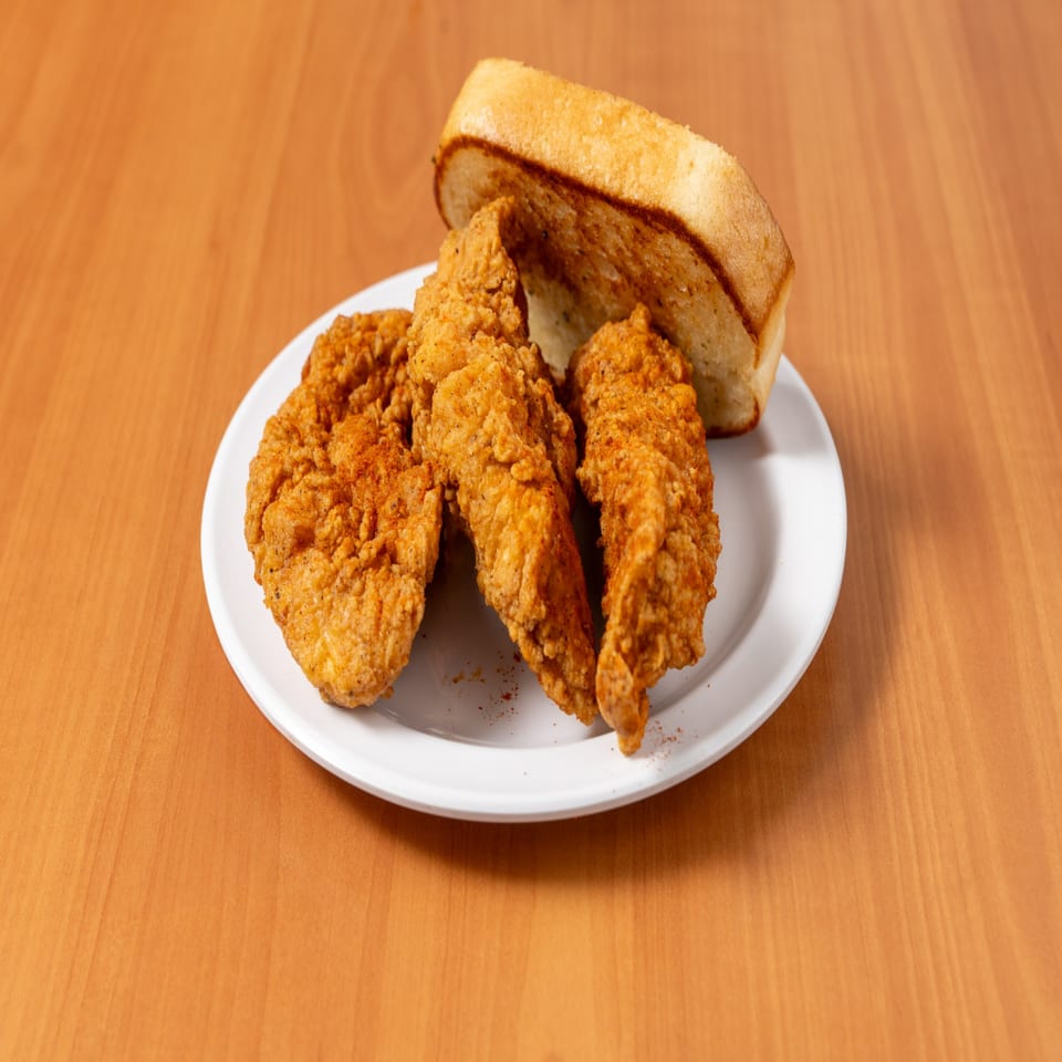 Three crispy fried chicken tenders and a slice of toasted bread on a white plate.