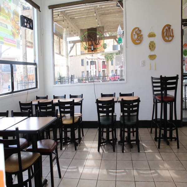 Empty restaurant interior with tables, chairs, large windows, and decorative wall hangings.