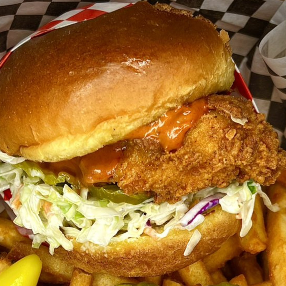 Krispi Hot Chicken sandwich with sauce, coleslaw, and pickles, served with fries in a basket.