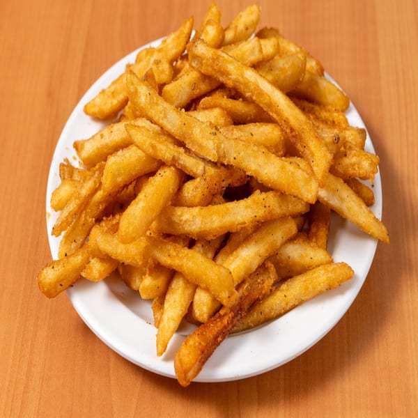 A white plate piled high with golden, seasoned french fries on a wooden table.