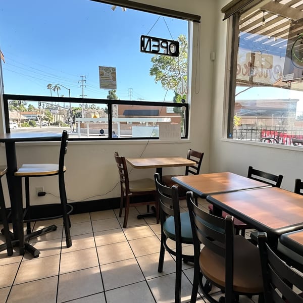 Interior of Krispi Hot Chicken with empty tables and chairs, and a street view through large windows.