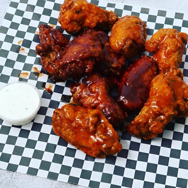 Krispi Hot Chicken wings, some with red sauce and some with dark sauce, on checkered paper with ranch.
