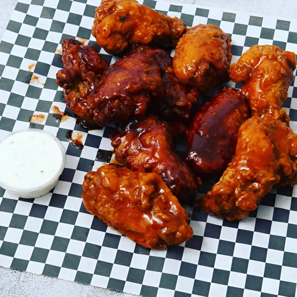 Krispi Hot Chicken wings, some with red sauce and some with dark sauce, on checkered paper with ranch.