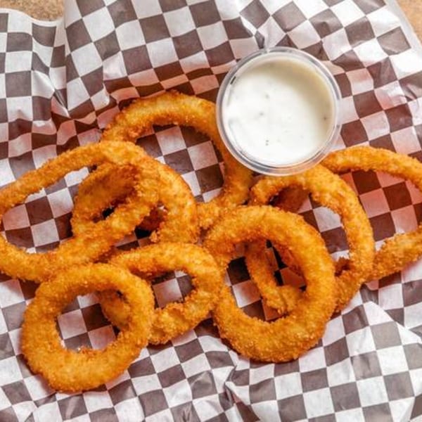 Golden-brown onion rings and a side of dipping sauce in a Krispi Hot Chicken basket.