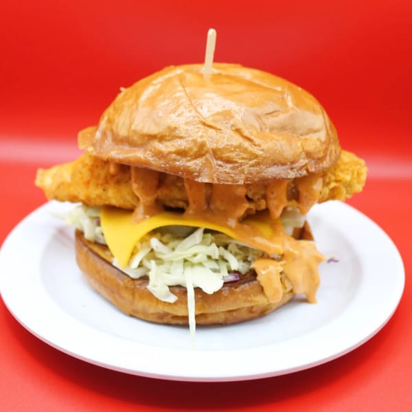 Krispi Hot Chicken sandwich with cheese, coleslaw, and sauce on a white plate against a red background.